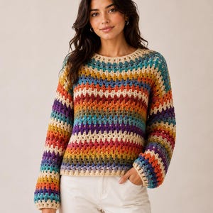 May include: A long-sleeved sweater featuring a multi-colored crochet granny square pattern. The garment displays horizontal stripes of cream, orange, red, purple, blue, and green yarn. It has a round neckline and ribbed cuffs at the wrists.