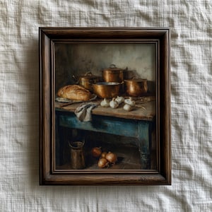 Könnte beinhalten: Ein gerahmtes Stillleben-Gemälde zeigt eine rustikale Küchenszene. Kupferkessel und eine Schüssel stehen auf einem blauen Tisch, zusammen mit einem Brotlaib, Knoblauch und Zwiebeln. Das Gemälde hat eine warme, Vintage-Ästhetik.