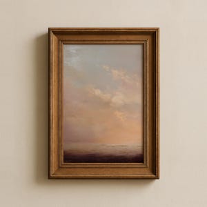 May include: A framed landscape painting with a warm color palette. The artwork depicts a serene sky with soft clouds in shades of peach, pink, and blue, above a misty horizon. The painting is encased in a wooden frame.