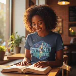 Op de afbeelding: Een marineblauw t-shirt met de tekst "EXTRA STRENGTH AUTISTIC" in een geometrisch ontwerp. De persoon draagt het t-shirt en leest een boek. De afbeelding is binnenshuis gemaakt, met natuurlijk licht en een warm kleurenpalet.