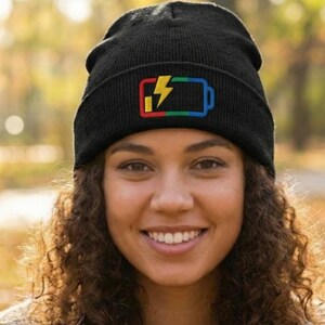 May include: Black beanie with a colorful battery and lightning bolt design. The beanie features a rectangular battery outline with a lightning bolt inside, colored in red, yellow, green, and blue. The beanie is made of a soft, knitted material.