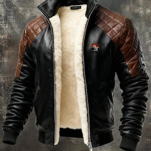 Peut inclure: Veste en cuir noire et marron avec un design matelassé aux épaules et une doublure en peau de mouton crème. La veste est dotée d'une fermeture éclair, d'un col montant et de poignets et d'ourlets côtelés. Un petit emblème est visible sur la poitrine.