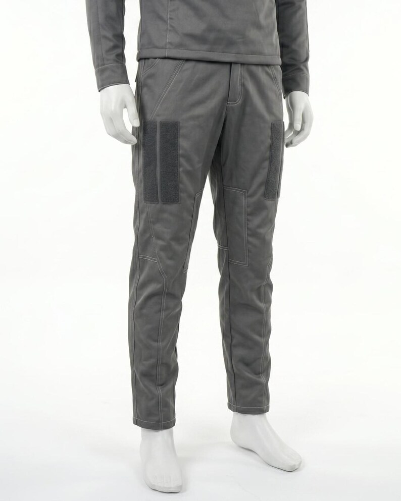 Puede incluir: Pantalones grises con dos parches rectangulares de color gris oscuro en la parte superior del muslo. Los pantalones tienen costuras visibles y forman parte de un conjunto gris a juego. Los pantalones se exhiben en un maniqu&iacute;.