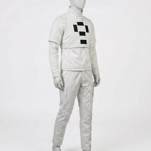 May include: A light grey futuristic costume displayed on a mannequin. The outfit includes a high-collared shirt with a black geometric design, a cropped jacket, and matching pants. The pants have pockets and the outfit is made of a smooth material.