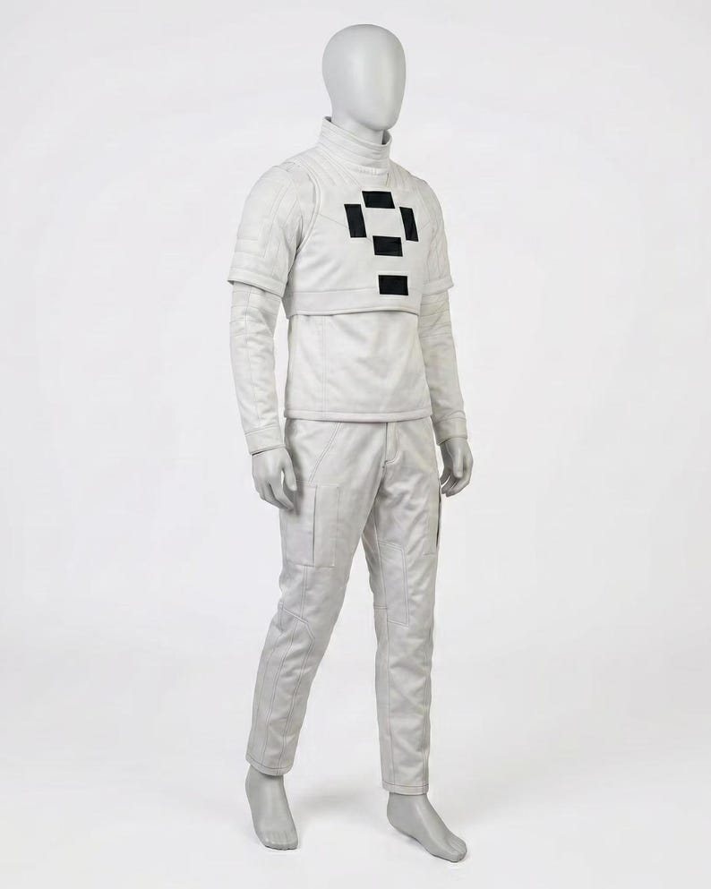 May include: A light grey futuristic costume displayed on a mannequin. The outfit includes a high-collared shirt with a black geometric design, a cropped jacket, and matching pants. The pants have pockets and the outfit is made of a smooth material.
