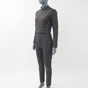 Op de afbeelding: Een donkergrijze tweedelige outfit op een mannequin. De set bestaat uit een top met hoge hals en lange mouwen en een bijpassende broek. De outfit heeft bruine accenten op de schouders, ellebogen en knie&euml;n. De broek heeft een getailleerd ontwerp.