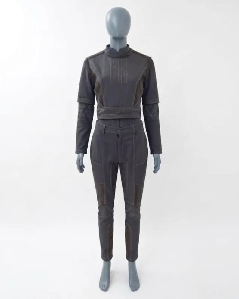 Op de afbeelding: Een tweedelige outfit in donkergrijs, getoond op een mannequin. De top is een cropped jasje met lange mouwen en een hoge kraag. De broek is getailleerd met patches op de knie&euml;n. De outfit heeft zichtbare stikseldetails.