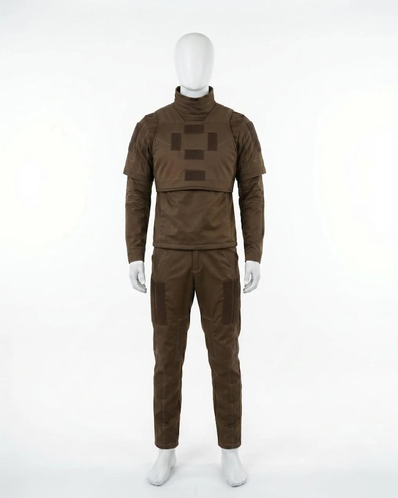 May include: A brown tactical uniform displayed on a mannequin. The outfit includes a long-sleeved shirt with a high collar, a chest plate, and matching pants. The uniform has several square patches and pockets.
