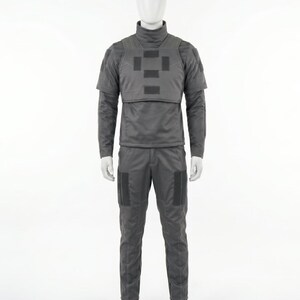 Puede incluir: Un uniforme t&aacute;ctico gris exhibido en un maniqu&iacute;. El conjunto incluye una camisa de manga larga con cuello alto, un chaleco con parches rectangulares y pantalones a juego con bolsillos en las rodillas. El uniforme est&aacute; dise&ntilde;ado para la funcionalidad.