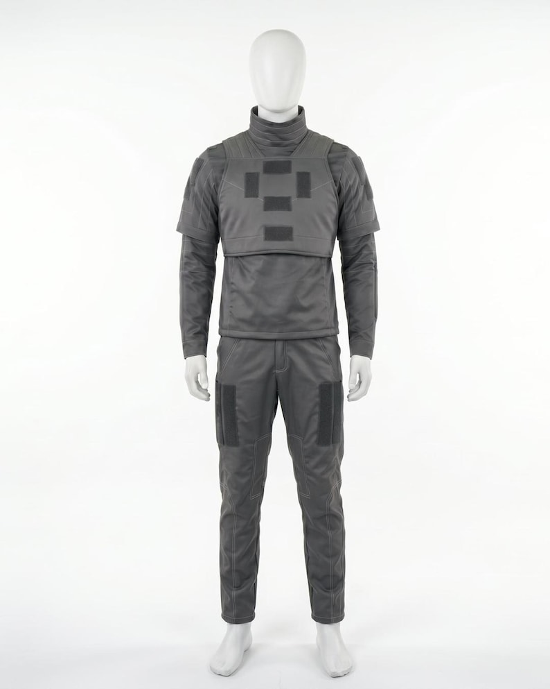 Puede incluir: Un uniforme t&aacute;ctico gris exhibido en un maniqu&iacute;. El conjunto incluye una camisa de manga larga con cuello alto, un chaleco con parches rectangulares y pantalones a juego con bolsillos en las rodillas. El uniforme est&aacute; dise&ntilde;ado para la funcionalidad.