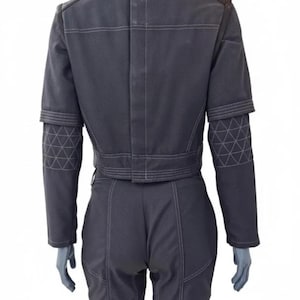 Op de afbeelding: Een donkergrijze jumpsuit met witte stiksels en geometrische patronen op de mouwen. De achterkant toont een getailleerde taille, schouderdetails en een hoge kraag. De outfit lijkt gemaakt van een duurzame stof.