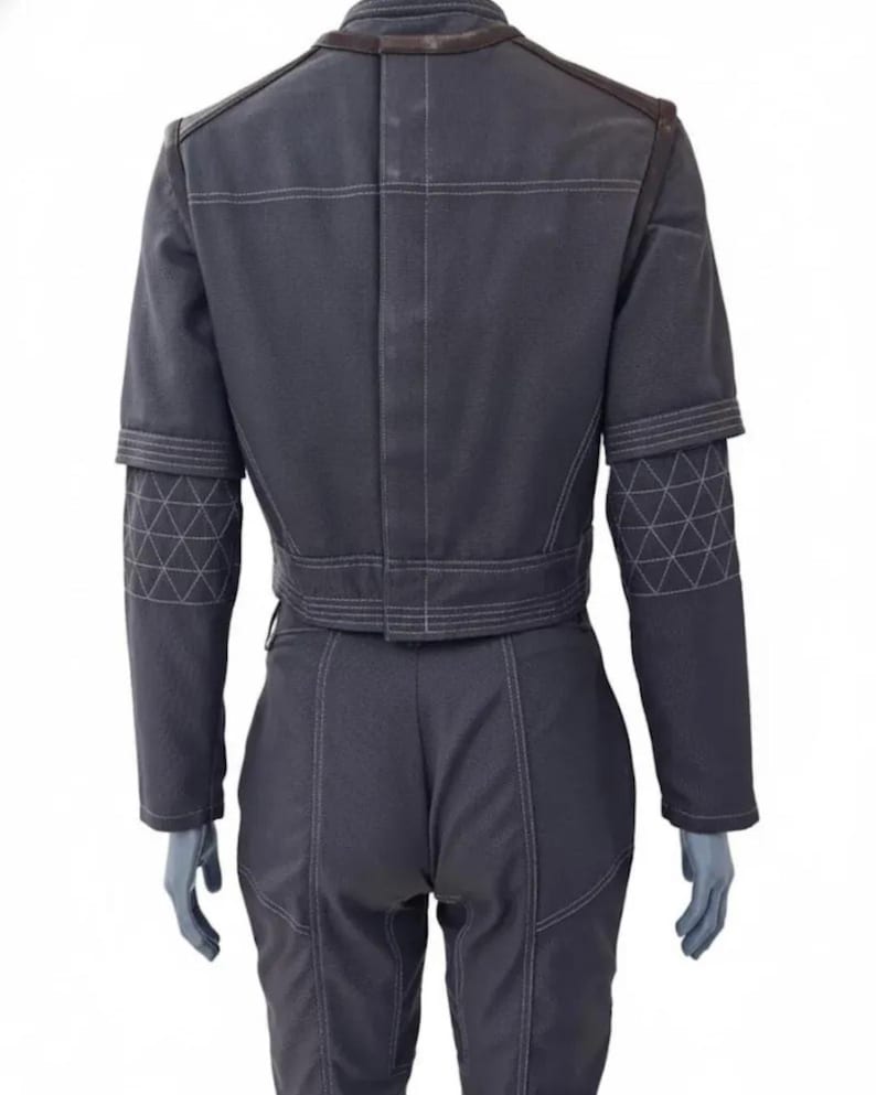 Op de afbeelding: Een donkergrijze jumpsuit met witte stiksels en geometrische patronen op de mouwen. De achterkant toont een getailleerde taille, schouderdetails en een hoge kraag. De outfit lijkt gemaakt van een duurzame stof.