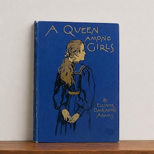 Könnte beinhalten: Ein blaues gebundenes Buch mit dem Titel A Queen Among Girls von Ellinor Davenport Adams. Das Cover zeigt eine goldfarbene Illustration einer Person mit langem Haar von hinten, die ein Kleid mit Kragen und einem Gürtel in der Taille trägt.