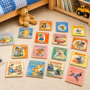 Könnte beinhalten: Eine Sammlung von Vintage-Kinderbüchern mit farbenfrohen Einbänden, darunter Titel wie "Puppy Tales", "Snow White" und "Woodland Babies". Die Bücher sind auf einem beigefarbenen Teppich in der Nähe eines Bettes und eines Teddybären angeordnet.