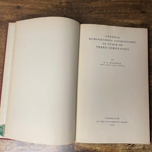 May include: An open book titled "General Homogeneous Coordinates in Space of Three Dimensions" by E.A. Maxwell, published by Cambridge at the University Press in 1951. The book is open on a wooden surface.