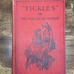 Puede incluir: Un libro rojo vintage titulado "Tickles or The School That Was Different". La portada presenta ilustraciones negras de dos figuras. El título está en negro, con comillas alrededor de "Tickles".