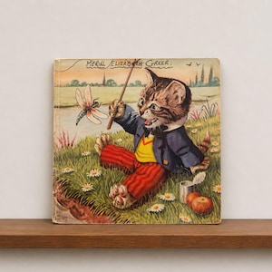 Può includere: Una copertina di un libro per bambini vintage con un gattino tigrato marrone che indossa una giacca blu, un gilet giallo e pantaloni a righe rosse. Il gattino tiene un bastoncino vicino a una libellula in un prato. Il testo Meriel Elizabeth Greer è stampato sopra.