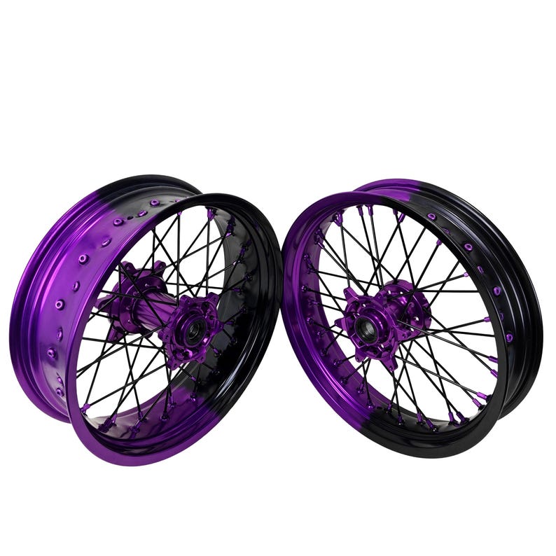 May include: Two motorcycle wheels with a striking color scheme. The rims are a vibrant purple, transitioning to black. The spokes and hubs are black and purple, creating a bold contrast. The wheels are designed for motorcycles.