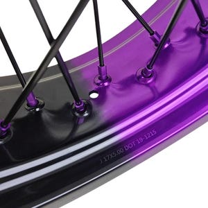 May include: Close-up of a motorcycle wheel rim with a two-tone design. The rim features a glossy purple finish on the inner section and a black outer section. Black spokes connect to the rim. The text "J 17X5.00 DOT 19-1215" is visible.
