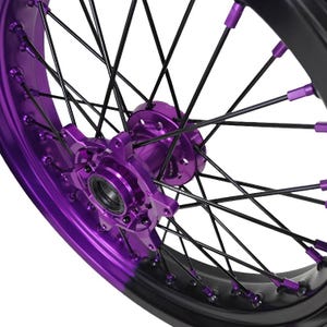 May include: Close-up of a motorcycle wheel with a black rim and spokes. The wheel features vibrant purple accents on the hub and spoke nipples, creating a striking contrast. The design is modern and eye-catching.
