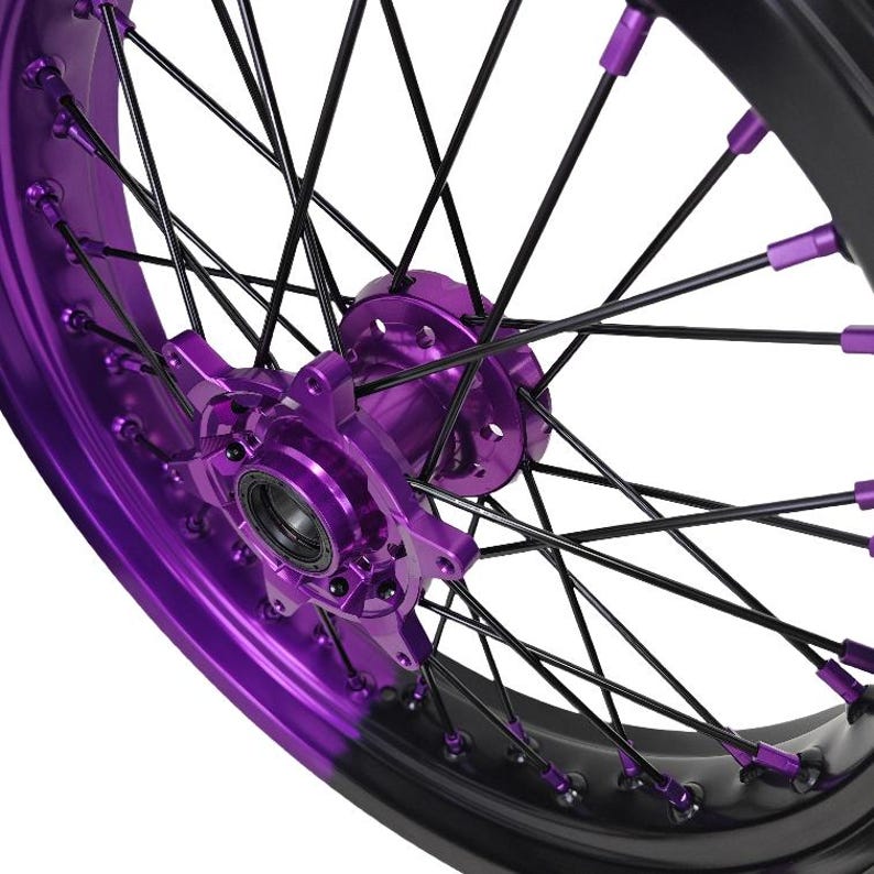May include: Close-up of a motorcycle wheel with a black rim and spokes. The wheel features vibrant purple accents on the hub and spoke nipples, creating a striking contrast. The design is modern and eye-catching.