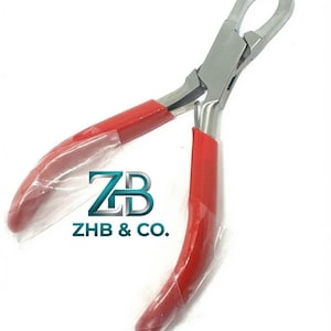 May include: Metal pliers featuring a silver-toned finish and bright red rubberised grips on the handles. The tool has curved, specialised jaws designed for gripping or bending. The text ZB ZHB & CO. is printed in blue and grey near the centre.