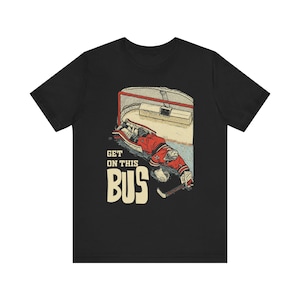 Puede incluir: Camiseta negra con una ilustración de un portero de hockey. El portero lleva equipo rojo y blanco y está tendido frente a la portería. El texto "GET ON THIS BUS" está impreso en un estilo vintage.