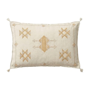 May include: Cream-colored rectangular pillow with a geometric pattern in gold and beige. The pillow has a textured surface and decorative tassels on the corners. The design features repeating cross-like shapes and a central arrow-like motif.