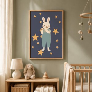 Op de afbeelding: Een ingelijste muurkunstprint met een crèmekleurig konijn in een lichtblauwe tuinbroek en een gestreept shirt, spelend op een houten fluit. Het konijn is omringd door gele sterren tegen een donkerblauwe achtergrond, in een houten lijst.