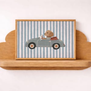 May include: A framed print featuring a light blue car with a dog driver. The car is set against a blue and white striped background. The dog is wearing a brown collar and driving the car. The frame is made of wood.