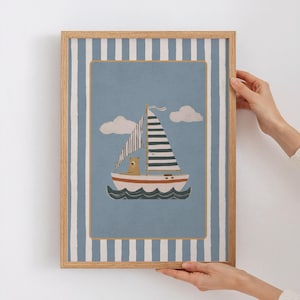 Puede incluir: Una impresión artística enmarcada con temática náutica. La obra presenta un velero con un oso, sobre un fondo azul con nubes blancas. El marco es marrón claro con un borde a rayas azules y blancas.