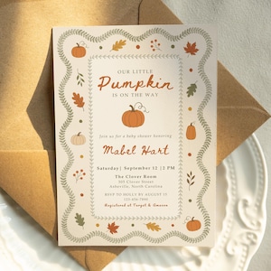 Puede incluir: Una tarjeta de invitación rectangular para baby shower con fondo crema y un borde decorativo de enredaderas verdes, calabazas naranjas y hojas de otoño. El texto dice: Our Little Pumpkin Is On The Way, en honor a Mabel Hart.