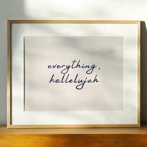Può includere: Una stampa artistica incorniciata che presenta il testo everything, hallelujah in una grafia corsiva blu scuro. La stampa è posta su uno sfondo beige chiaro ed è racchiusa in una semplice cornice di legno chiaro con un bordo bianco.