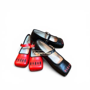 May include: Three Mary Jane shoes with buckled straps and rounded toes. One pair is black with red cutout details on the toe, and one single shoe is red with black cutout details. The text Caligar Craft is visible on the black shoe.