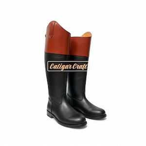 Könnte beinhalten: Ein Paar hohe schwarze Reitstiefel mit braunen Lederoberteilen. Die Stiefel haben ein klassisches Design mit glatter, polierter Oberfläche. Der Text "Caligar Craft" ist auf den Stiefeln zu sehen.