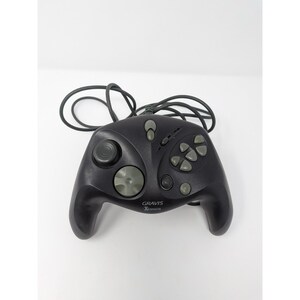 May include: A black Gravis Xterminator gamepad with gray buttons and a directional pad. The controller has a joystick, several buttons, and a long black cord. The Gravis logo is visible on the front of the controller.