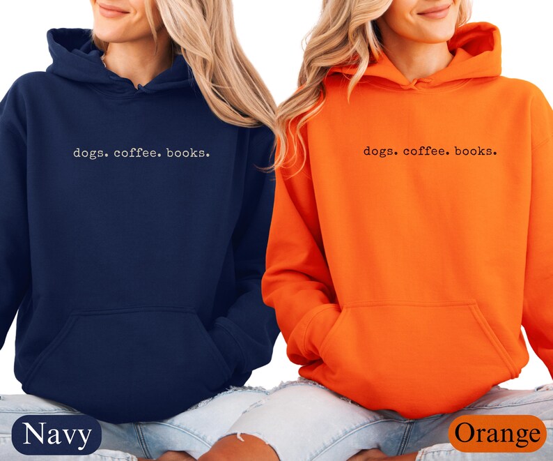 May include: Two hooded sweatshirts, one navy blue and one orange, are displayed. Each sweatshirt has a front pocket and the phrase "dogs. coffee. books." printed in a simple font across the chest. The navy sweatshirt is labeled "Navy" and the orange sweatshirt is labeled "Orange".
