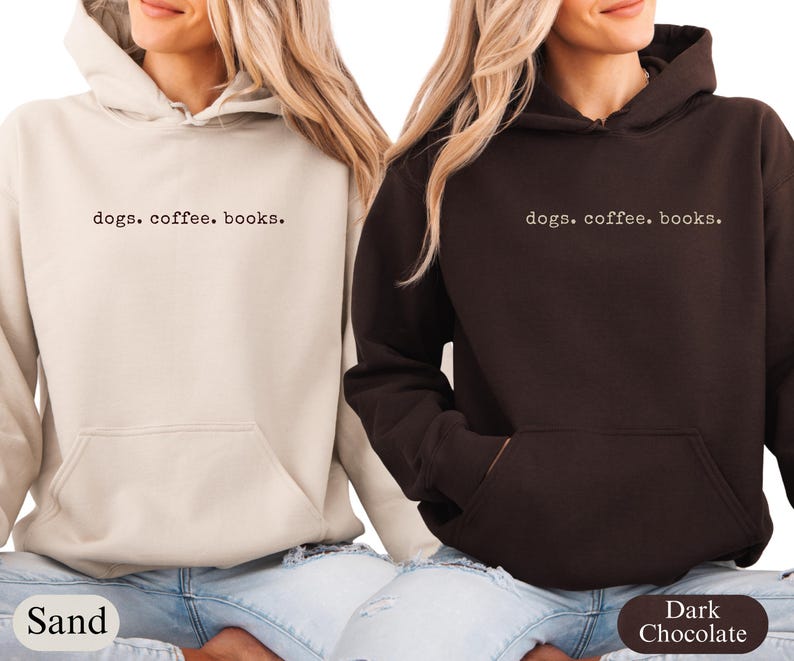 May include: Two hooded sweatshirts, one sand-colored and one dark chocolate, with the text "dogs. coffee. books." printed in a simple font. Both sweatshirts have a front pocket and a drawstring hood. The models are wearing blue jeans.