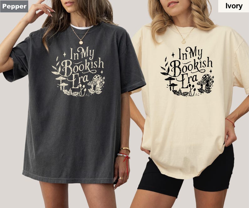 May include: Two oversized t-shirts, one pepper-colored and one ivory, are displayed. Each shirt features the text "In My Bookish Era" in a whimsical font, surrounded by botanical illustrations. The shirts are casual and comfortable.