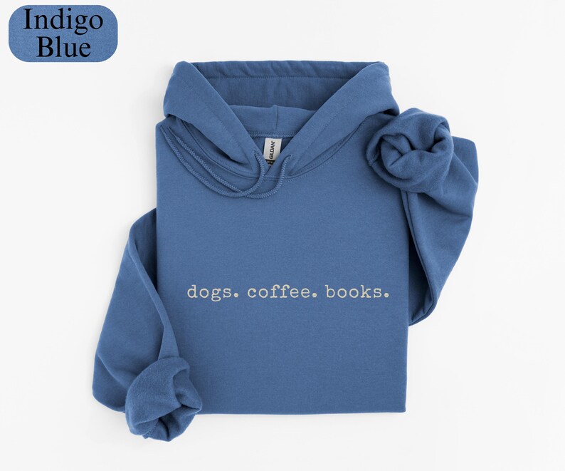 May include: Indigo blue hoodie with the words "dogs. coffee. books." in a simple font. The hoodie is folded neatly, with the hood and sleeves visible. The top left corner has a blue oval with the words "Indigo Blue".