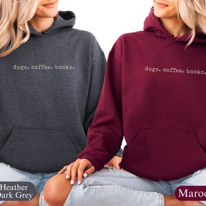 May include: Two hooded sweatshirts, one heather dark gray and one maroon, each with the text "dogs. coffee. books." in a simple, white font. The sweatshirts have a front pocket and a drawstring hood.