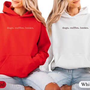 May include: Two hooded sweatshirts, one red and one white, with the text "dogs. coffee. books." printed in a small, centered font. Both sweatshirts have a front pocket and are worn with blue jeans.