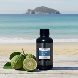 May include: A black bottle of "Sea of Dokdo" reed diffuser fragrance oil with a label. The image includes green citrus fruits and leaves, with a sliced fruit revealing the interior. The background shows a beach and ocean.