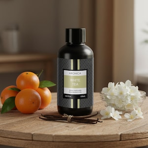May include: A black reed diffuser fragrance oil bottle with the text "White Tea" and "Aronica". The bottle is surrounded by oranges, vanilla beans, and white flowers in a glass bowl. The bottle contains 4.05 fl oz (120ml).