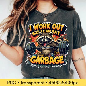 Puede incluir: Camiseta gris oscuro con un mapache de dibujos animados levantando pesas. El texto dice "I WORK OUT SO I CAN EAT GARBAGE". El mapache está rodeado de basura, el texto es amarillo y naranja.