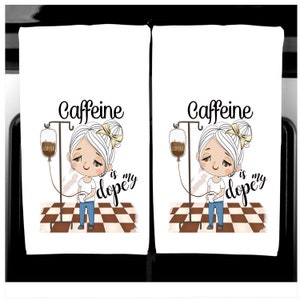 K&ouml;nnte beinhalten: Zwei wei&szlig;e K&uuml;chent&uuml;cher mit einer Cartoon-Illustration. Das Design zeigt ein M&auml;dchen mit einem Kaffee-IV-Tropf, dem Text "Caffeine is my dopey". Das M&auml;dchen h&auml;lt eine Kaffeetasse und steht auf einem braun-wei&szlig; karierten Boden.