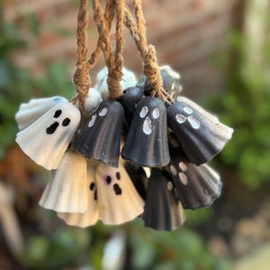 Könnte beinhalten: Eine Sammlung handgefertigter Geisterornamente in Schwarz und Weiß. Jeder Geist hat ein einfaches Gesichtsdesign. Sie sind an Naturfaser-Schnüren aufgehängt, ideal für Halloween-Dekorationen.