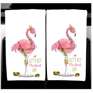 K&ouml;nnte beinhalten: Zwei wei&szlig;e K&uuml;chent&uuml;cher mit einem rosa Flamingo in einem Martini-Glas, garniert mit Oliven. Der Flamingo tr&auml;gt eine Krone und einen Schal. Der Text lautet "LET'S GET FLOCKED UP!" in Rosa. Gr&uuml;ne Oliven sind verstreut.