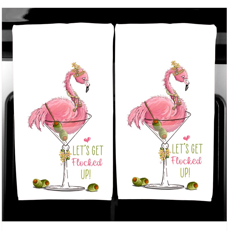K&ouml;nnte beinhalten: Zwei wei&szlig;e K&uuml;chent&uuml;cher mit einem rosa Flamingo in einem Martini-Glas, garniert mit Oliven. Der Flamingo tr&auml;gt eine Krone und einen Schal. Der Text lautet "LET'S GET FLOCKED UP!" in Rosa. Gr&uuml;ne Oliven sind verstreut.