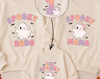Può includere: Tre felpe e un body color crema con grafiche di fantasmi. Le maglie per adulti riportano le scritte SPOOKY DADA e SPOOKY MAMA. Il body riporta ONE SPOOKY GHOUL. Un inserto circolare mostra il retro con il nome SOPHIA e il numero 1.